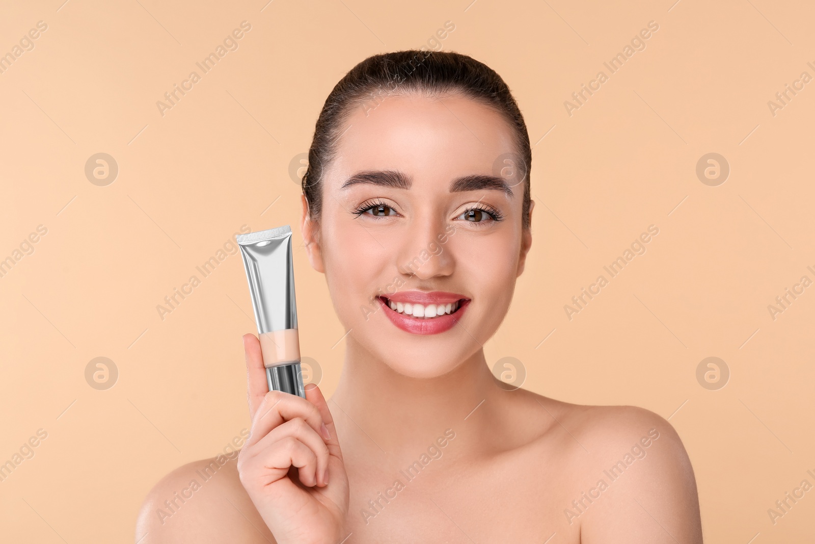 Photo of Woman holding tube of foundation on beige background