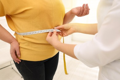 Image of Nutritionist measuring overweight woman's waist with tape in clinic, closeup