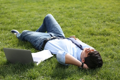 Young man lying on green lawn in park. Joy in moment