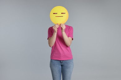 Photo of Woman holding emoticon with closed eyes and mouth on grey background