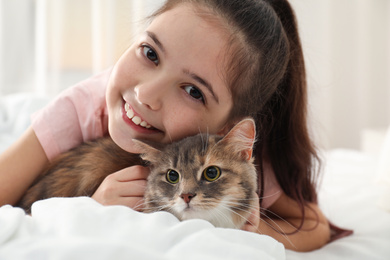 Cute little girl with cat lying on bed at home. First pet