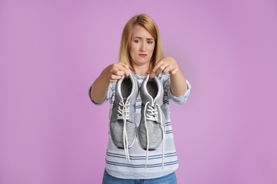 Photo of Young woman with stinky shoes on color background. Air freshener