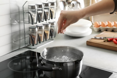 Woman salting boiling water in pot on stove, closeup