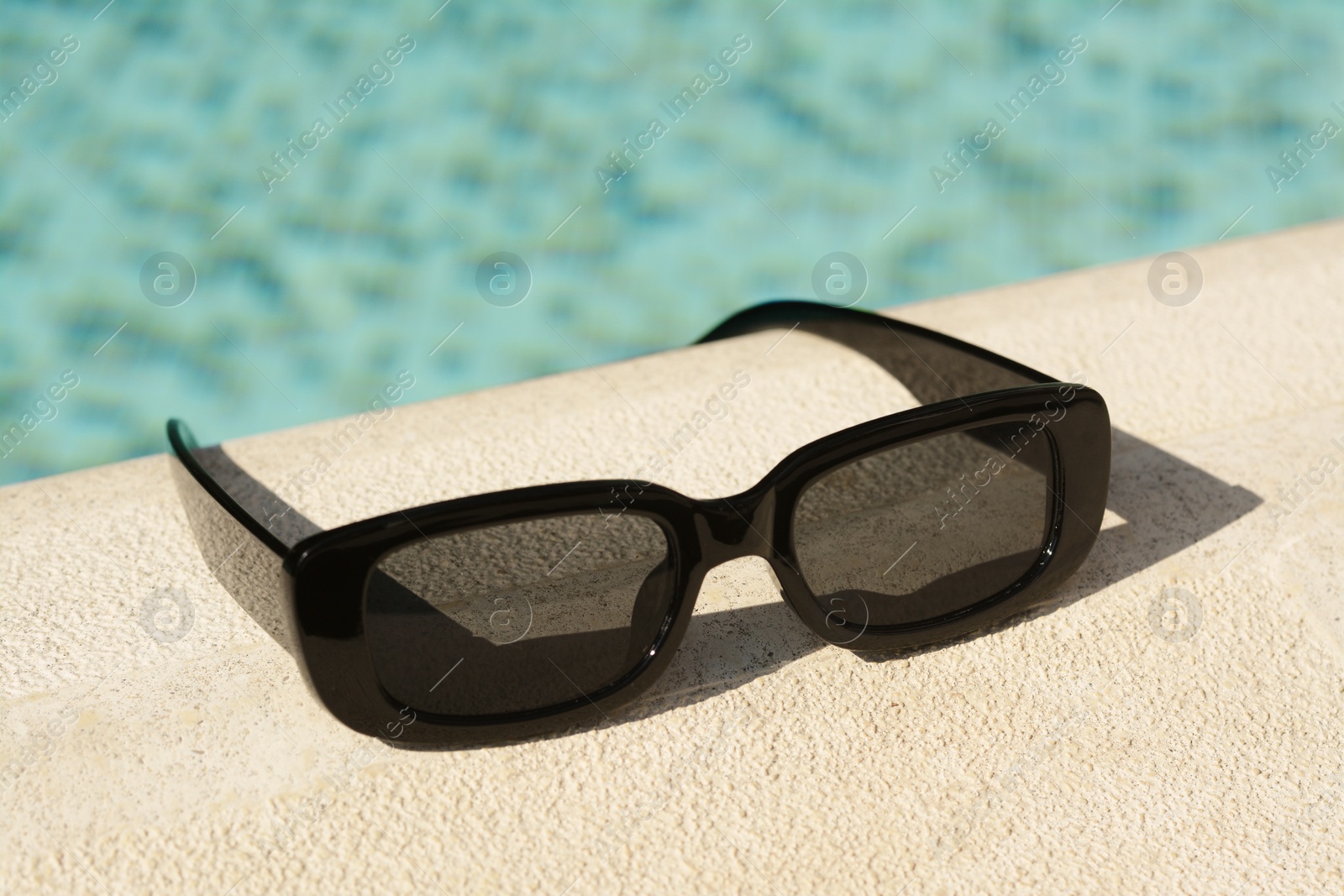 Photo of Stylish sunglasses near outdoor swimming pool on sunny day, closeup