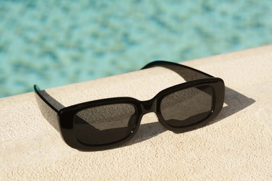 Stylish sunglasses near outdoor swimming pool on sunny day, closeup