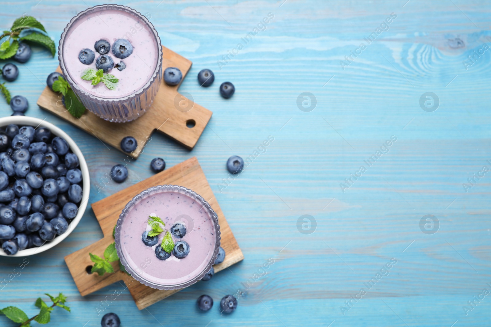 Photo of Glasses of blueberry smoothie with mint and fresh berries on light blue wooden table, flat lay. Space for text