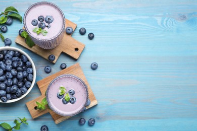 Photo of Glasses of blueberry smoothie with mint and fresh berries on light blue wooden table, flat lay. Space for text