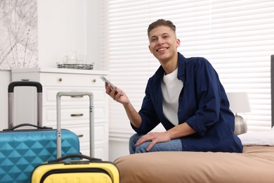 Photo of Smiling guest with smartphone on bed in stylish hotel room