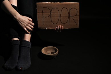 Woman holding cardboard sign with word "POOR" on dark background, closeup