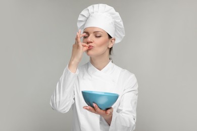 Photo of Woman chef in uniform holding bowl and showing perfect sign on grey background