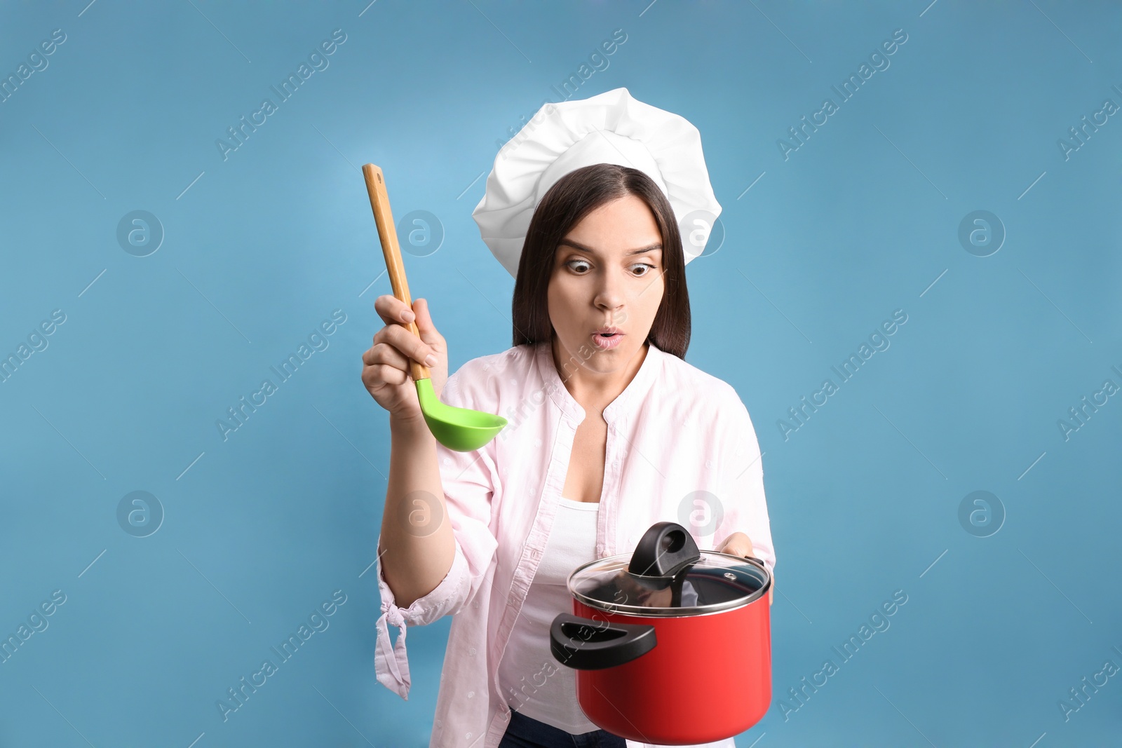 Photo of Surprised young woman with cooking pot and ladle on light blue background