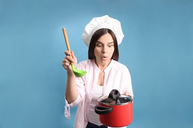 Surprised young woman with cooking pot and ladle on light blue background