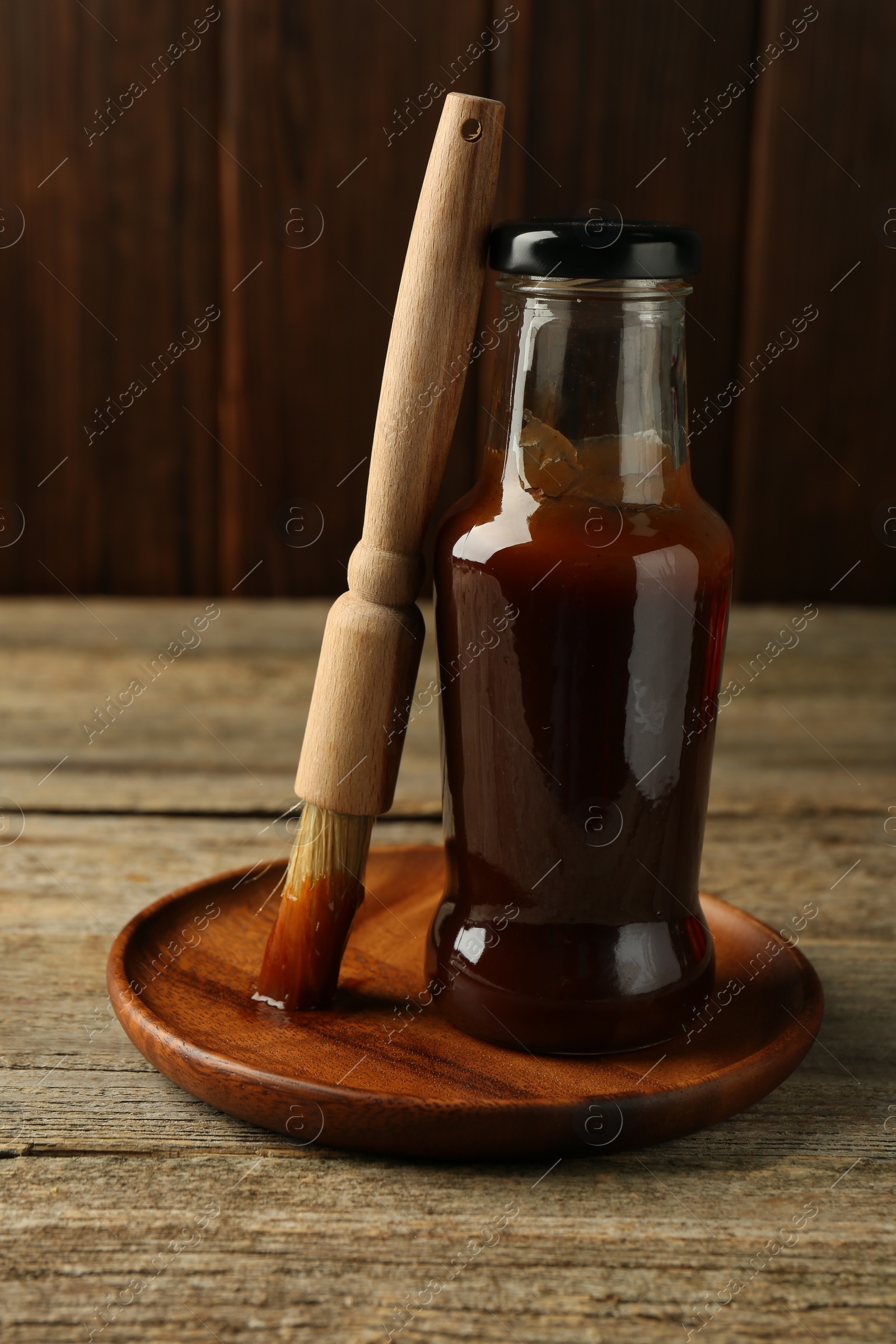 Photo of Tasty barbeque sauce in bottle and brush on wooden table