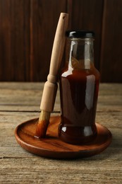 Photo of Tasty barbeque sauce in bottle and brush on wooden table