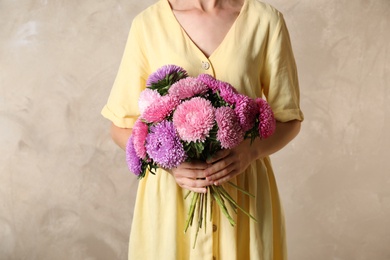 Woman holding bouquet of beautiful aster flowers on beige background, closeup