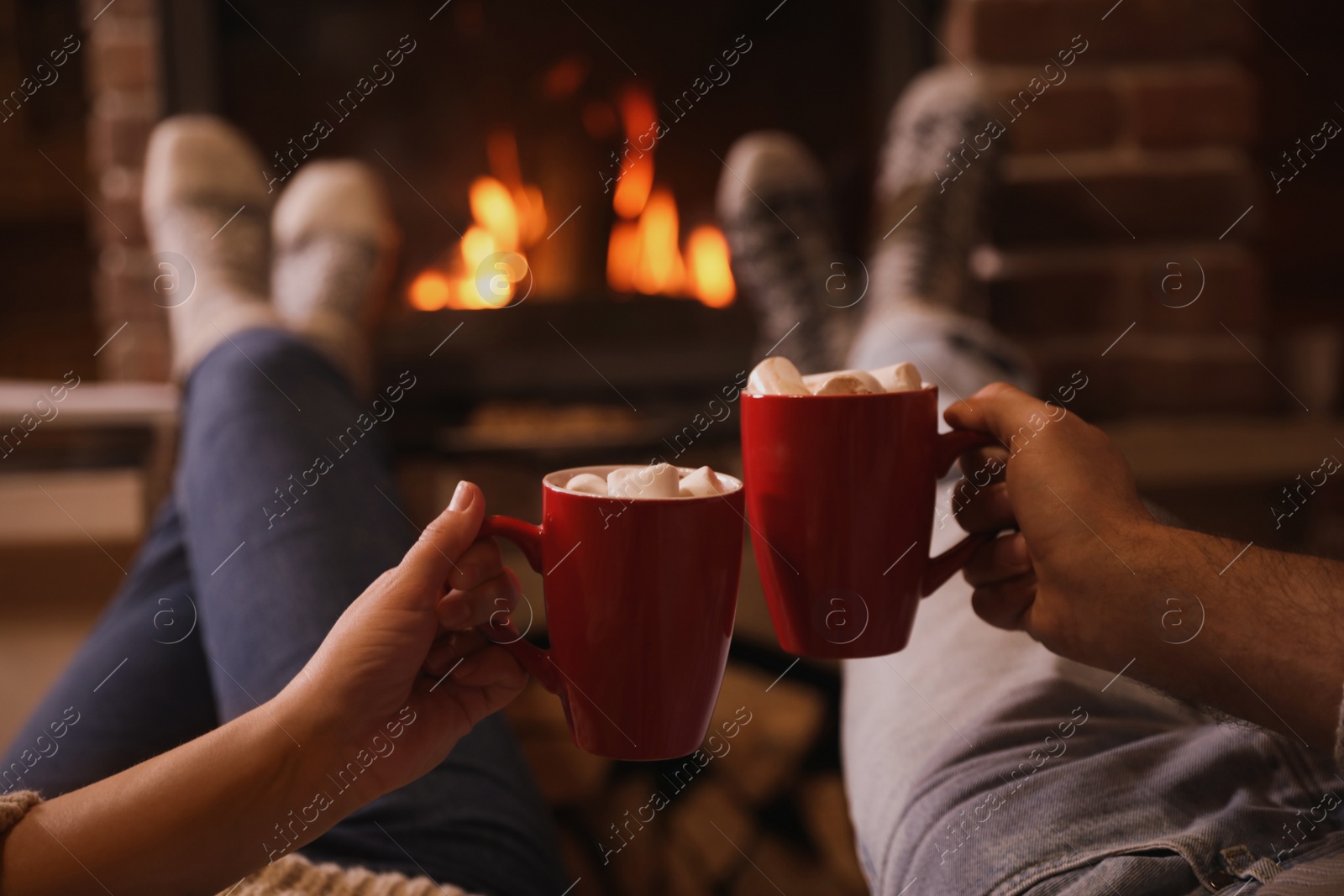 Photo of Lovely couple with sweet cocoa near fireplace indoors, closeup