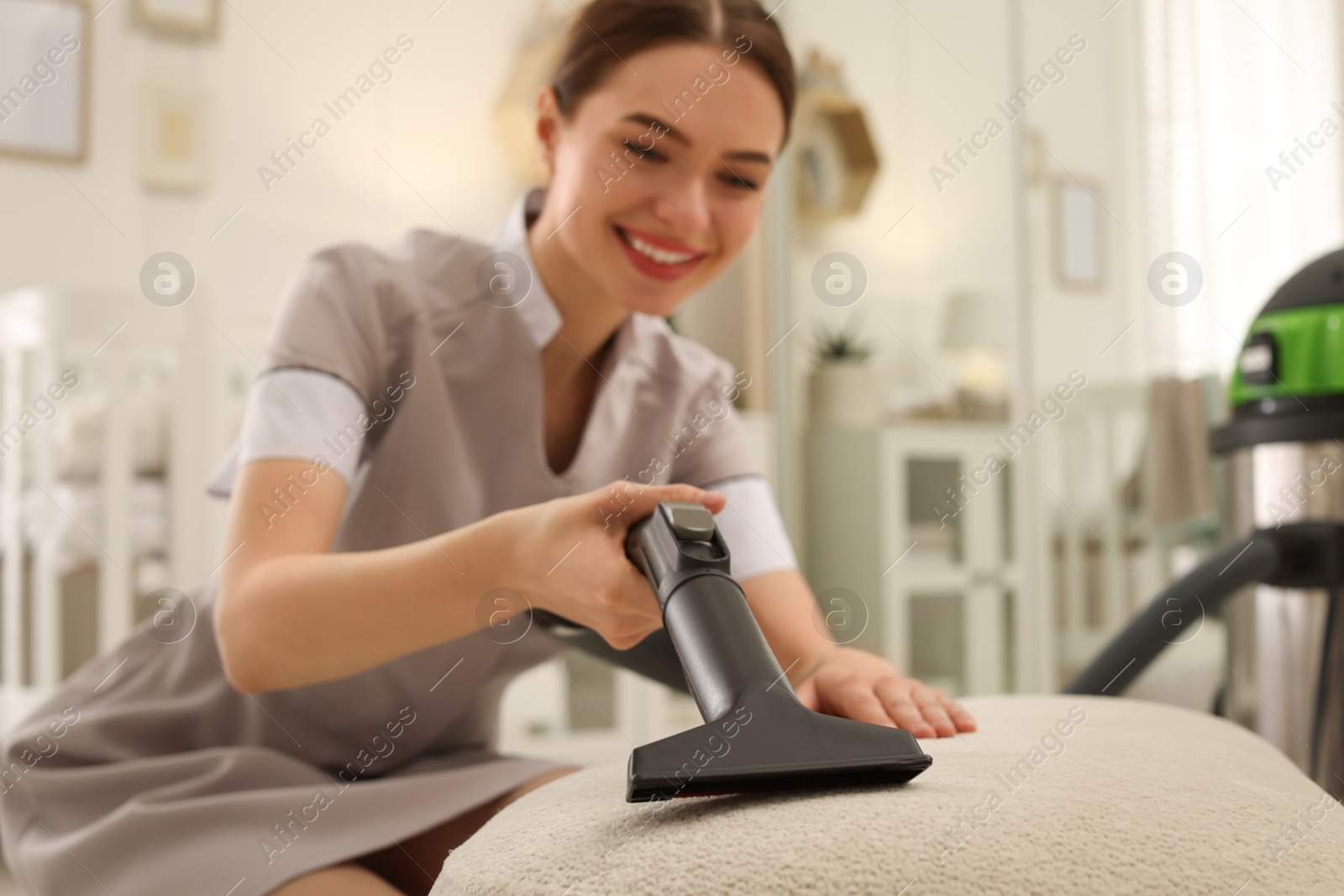 Photo of Professional chambermaid vacuuming pouf indoors, focus on nozzle