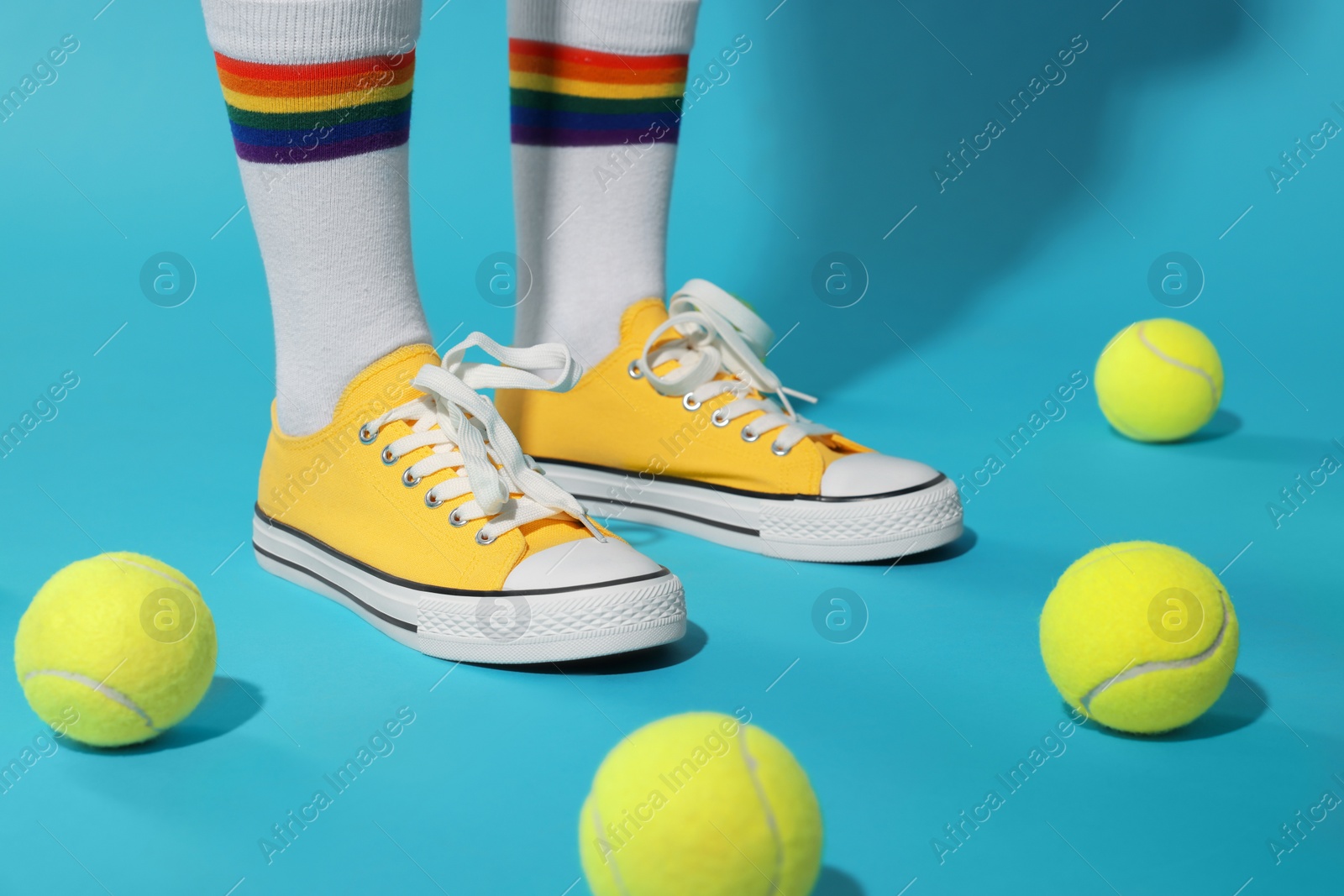 Photo of Woman wearing yellow classic old school sneakers and tennis balls on light blue background, closeup