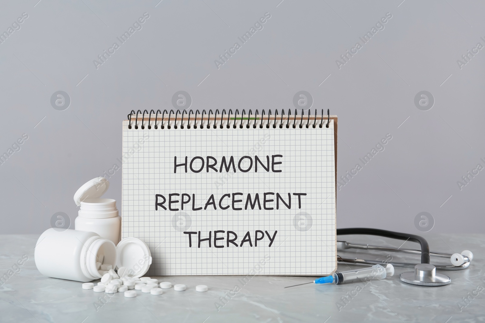 Image of Notebook with text Hormone Replacement Therapy, pills, stethoscope and syringes on light grey marble grey table