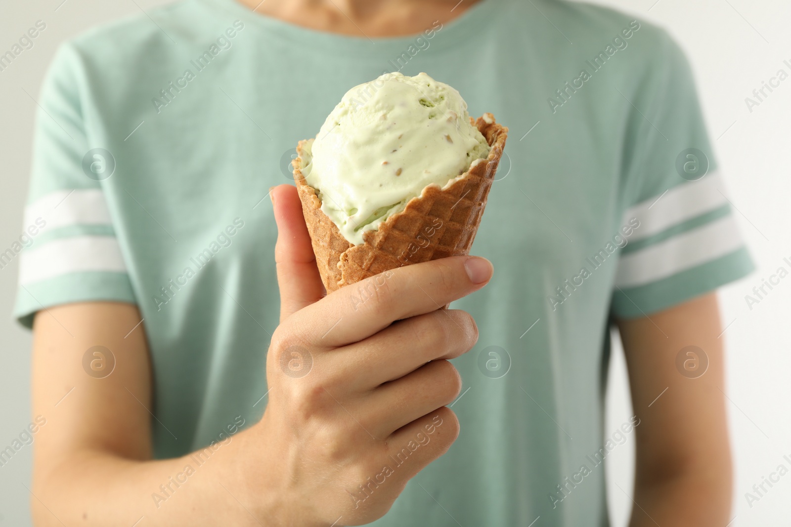 Photo of Woman holding green ice cream in wafer cone on light background, closeup