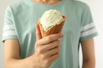 Photo of Woman holding green ice cream in wafer cone on light background, closeup