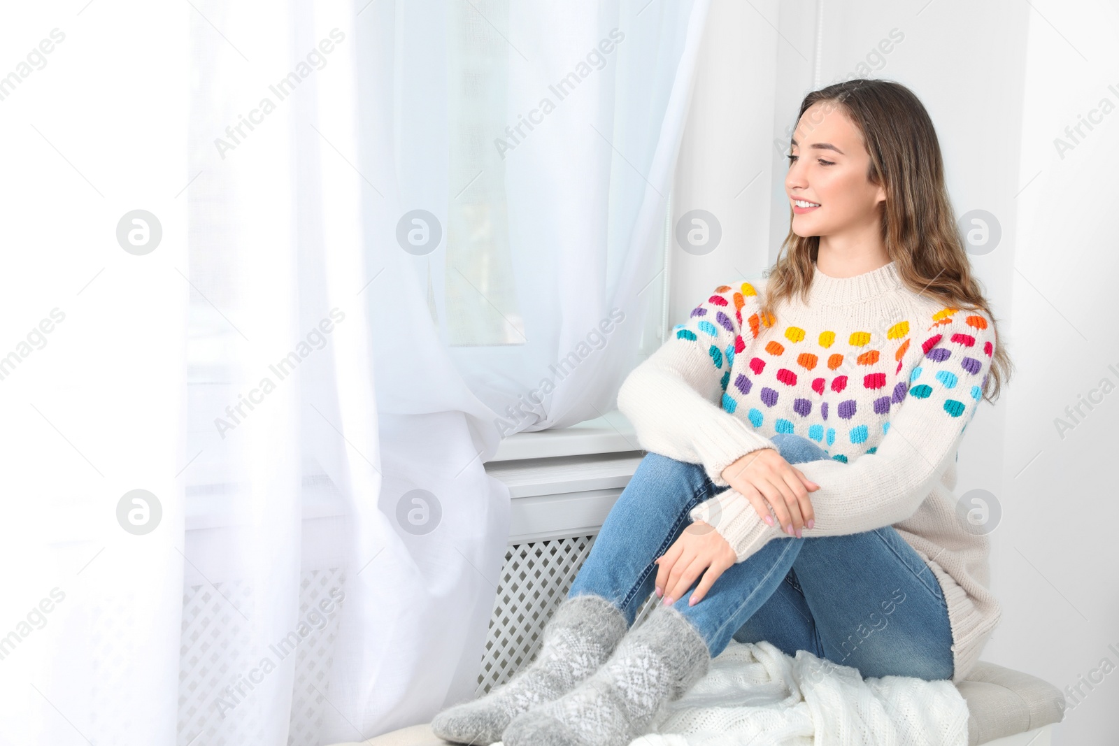 Photo of Beautiful teenage girl in warm cozy sweater looking out window at home. Space for text