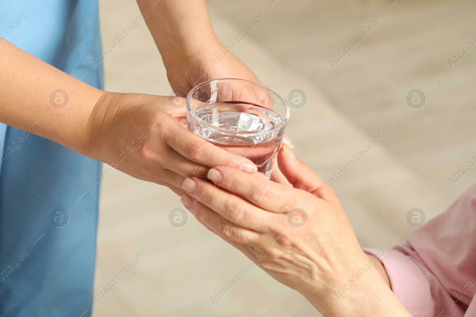 Photo of Caretaker giving glass of water to elderly woman indoors, closeup