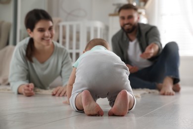 Happy parents watching their baby crawl on floor at home