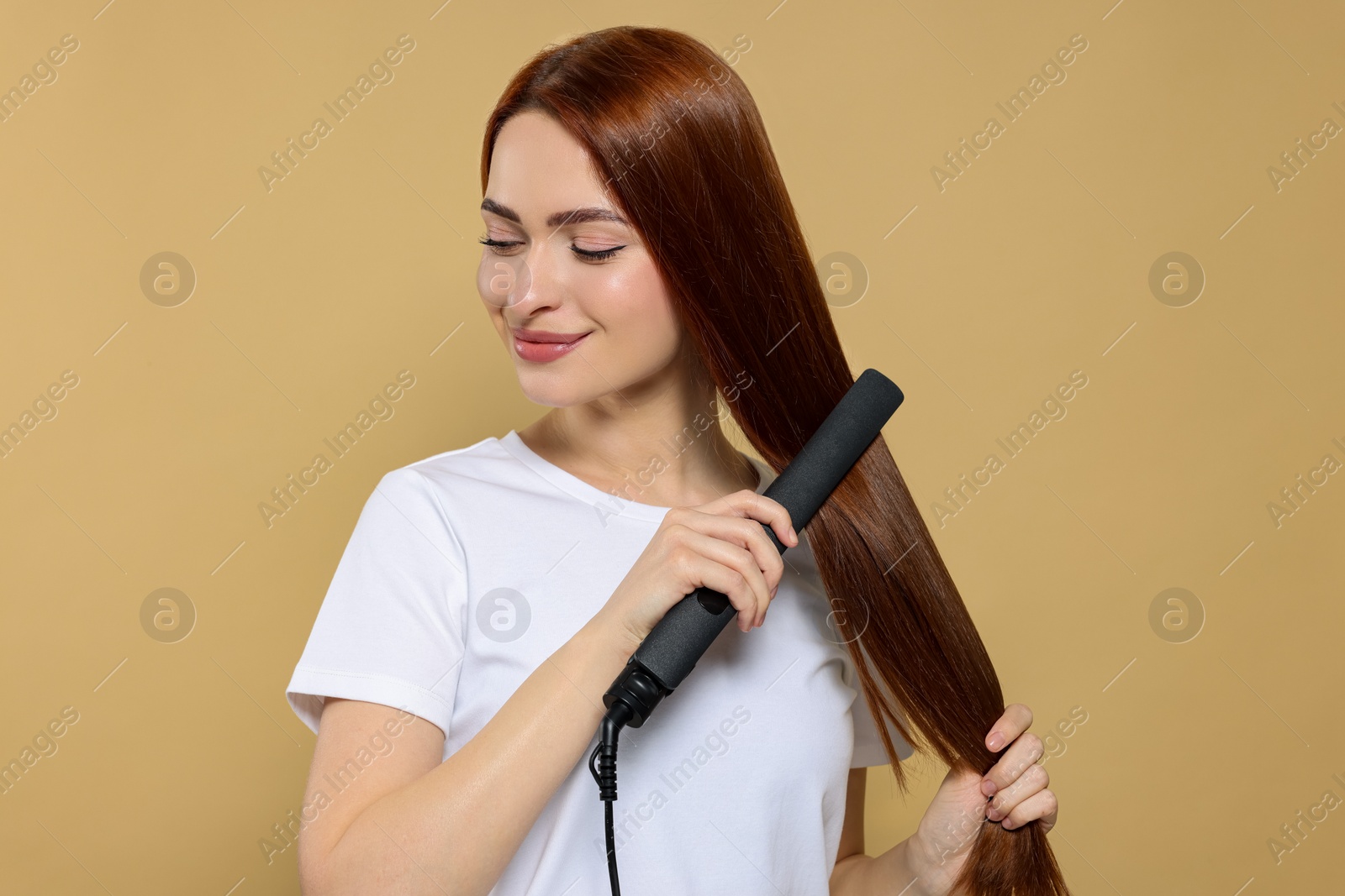 Photo of Beautiful woman using hair iron on beige background