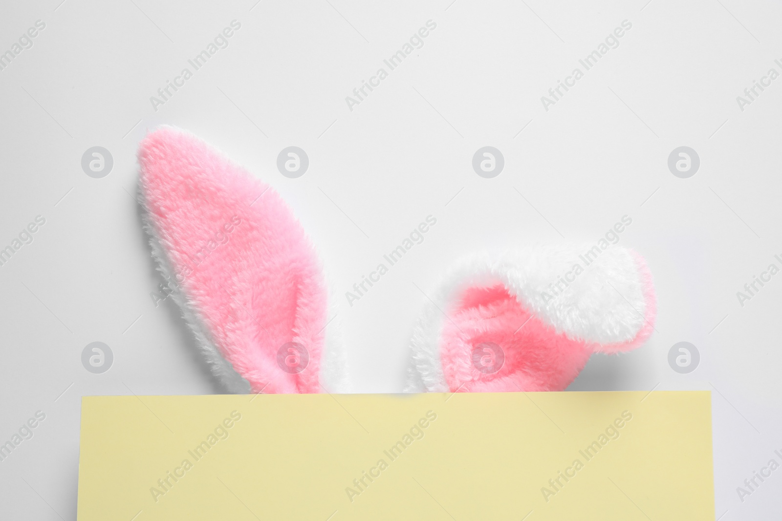 Photo of Decorative bunny ears and yellow card on white background, top view. Easter holiday