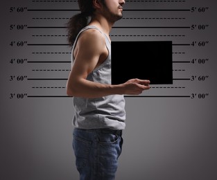 Criminal mugshot. Arrested man with blank card against height chart, closeup