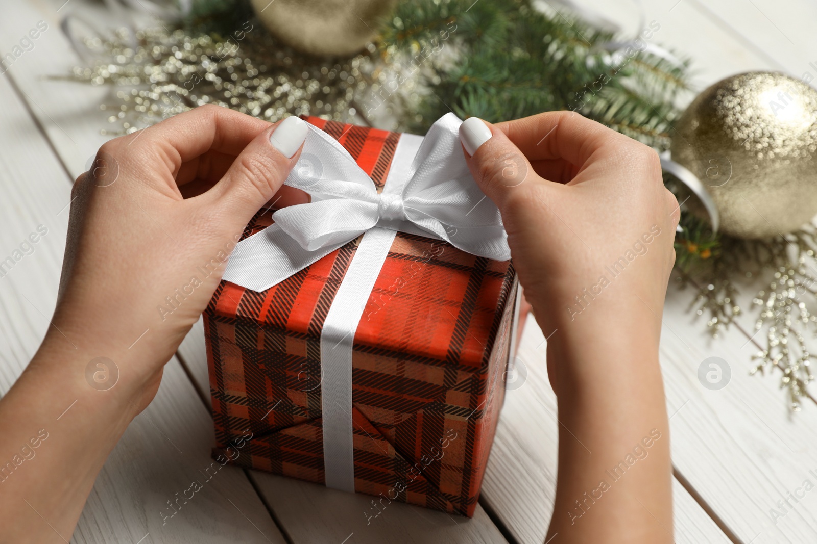 Photo of Woman wrapping Christmas gift at white wooden table, closeup