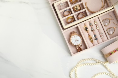 Photo of Jewelry box with stylish golden bijouterie on white marble table, flat lay. Space for text