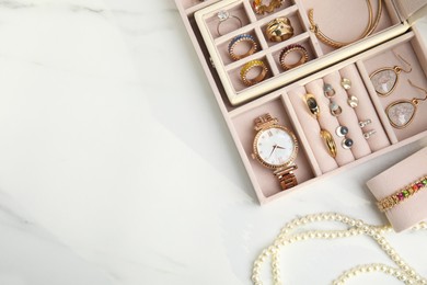 Jewelry box with stylish golden bijouterie on white marble table, flat lay. Space for text