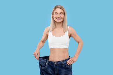Slim woman wearing big jeans on light blue background. Weight loss