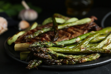 Tasty asparagus with grilled meat on slate board, closeup