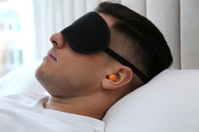 Photo of Man with foam ear plugs and mask sleeping in bed, closeup