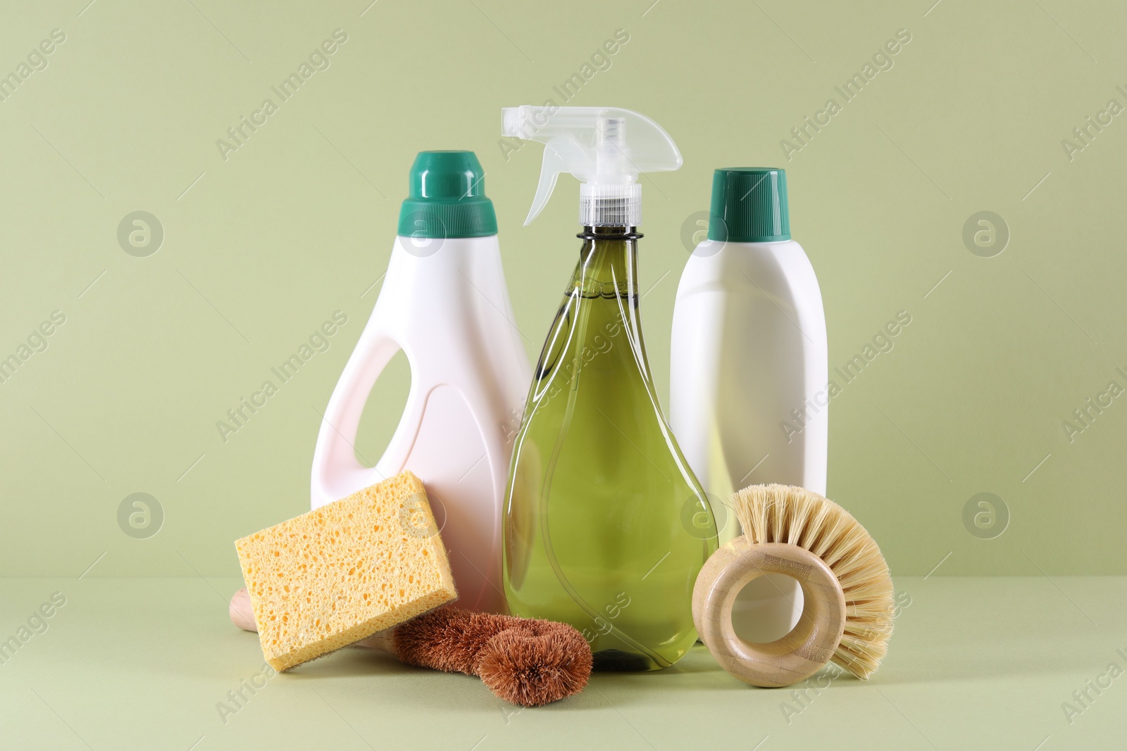 Photo of Bottles of cleaning product, brushes and sponge on light green background