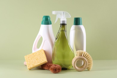 Bottles of cleaning product, brushes and sponge on light green background