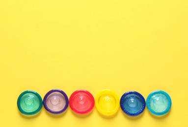 Colorful condoms on yellow background, flat lay. Space for text