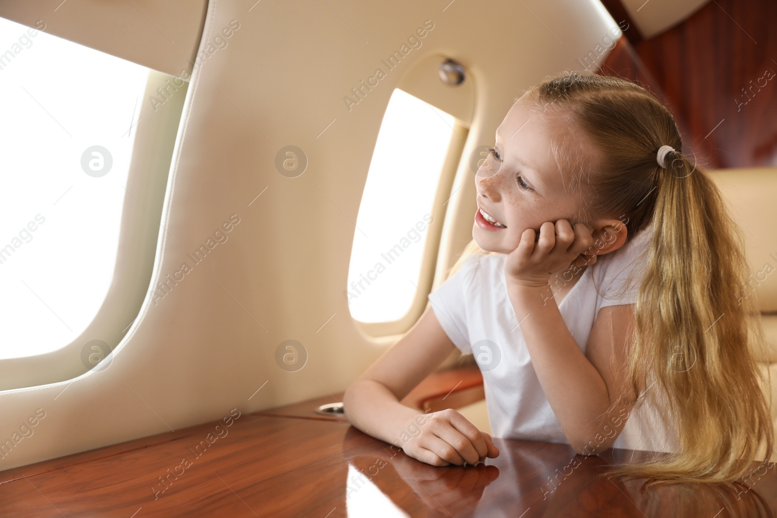 Photo of Cute little girl looking out window at table in airplane during flight