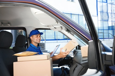 Photo of Young courier with clipboard and parcels in delivery car