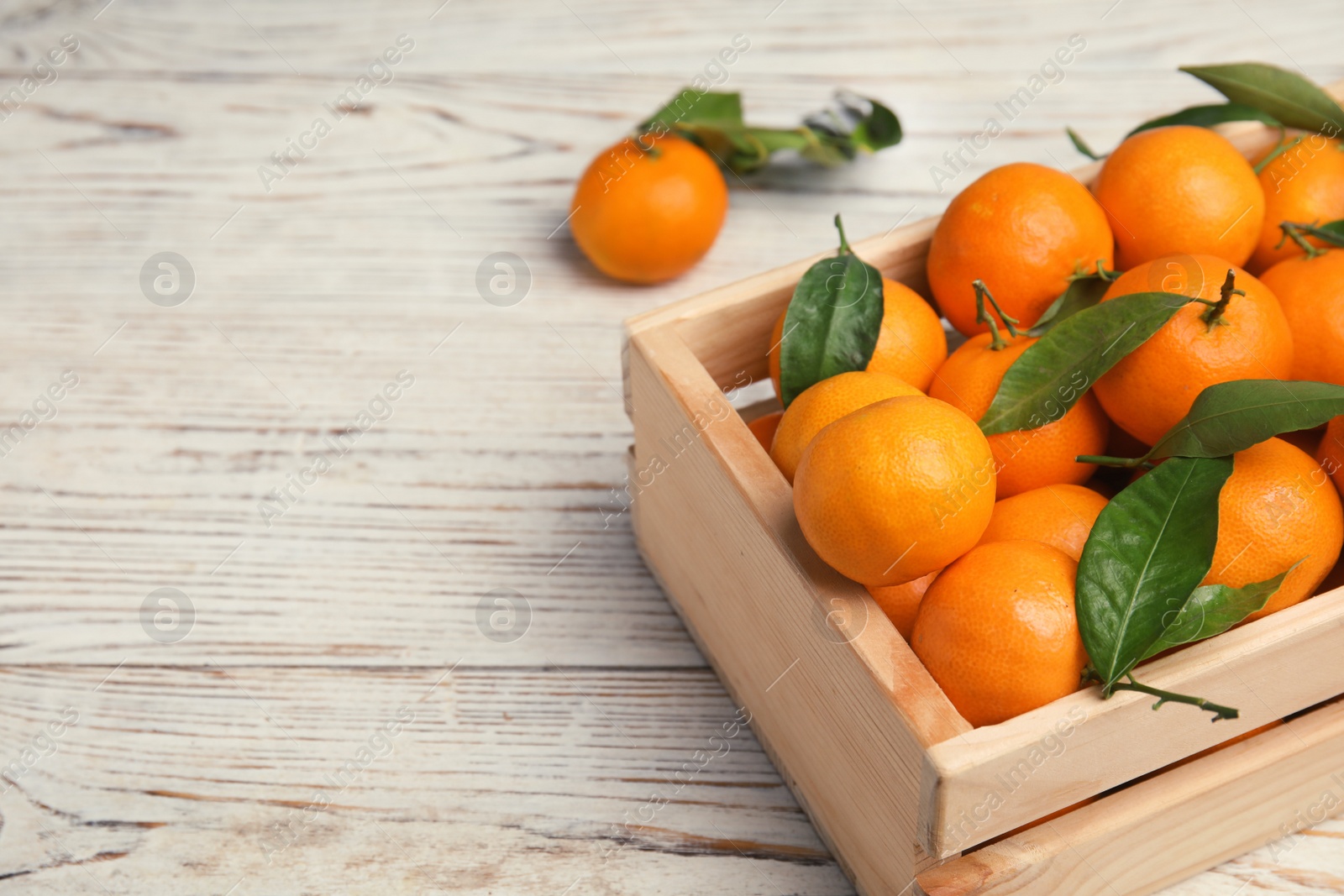 Photo of Fresh ripe tangerines in wooden crate on table. Space for text