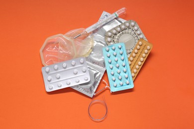 Photo of Contraceptive pills, condoms, intrauterine device and thermometer on orange background, flat lay. Different birth control methods
