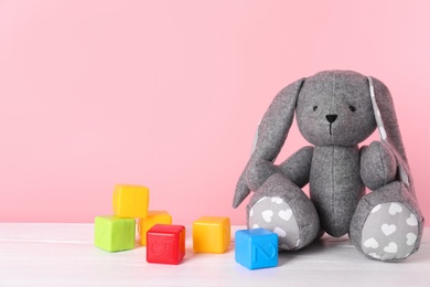 Photo of Adorable toy bunny and plastic cubes on table against color background, space for text. Child room elements