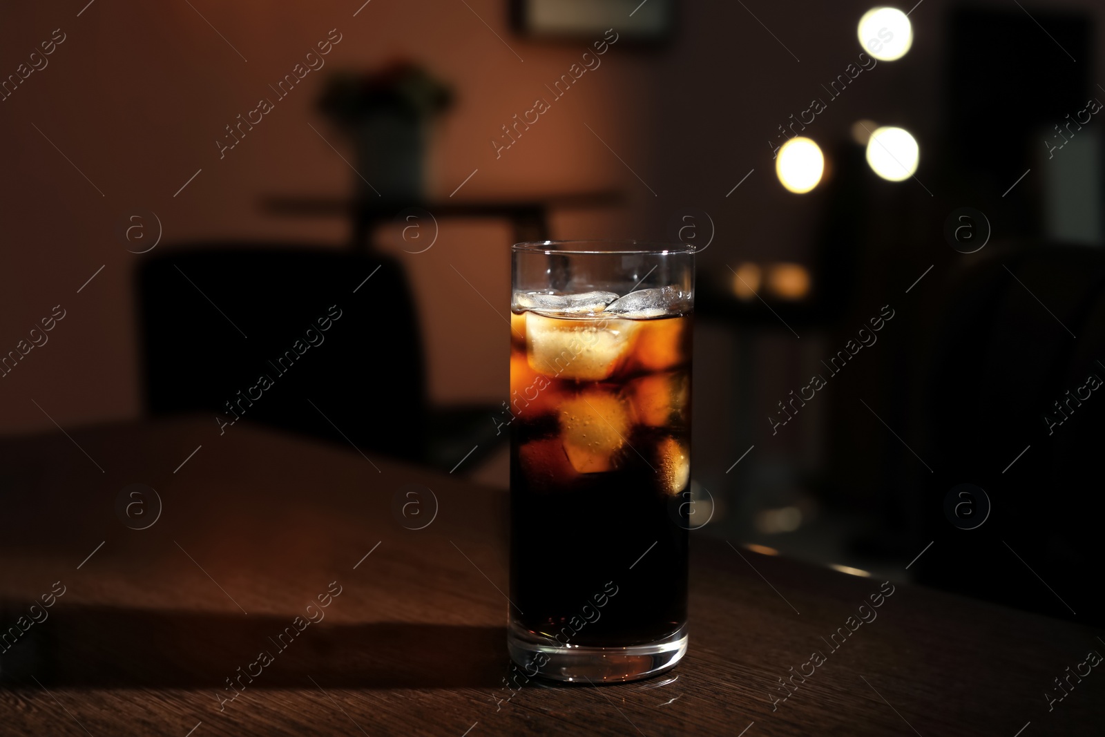 Photo of Glass of cold cola on table in dark room