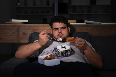 Photo of Depressed overweight man eating sweets in living room at night