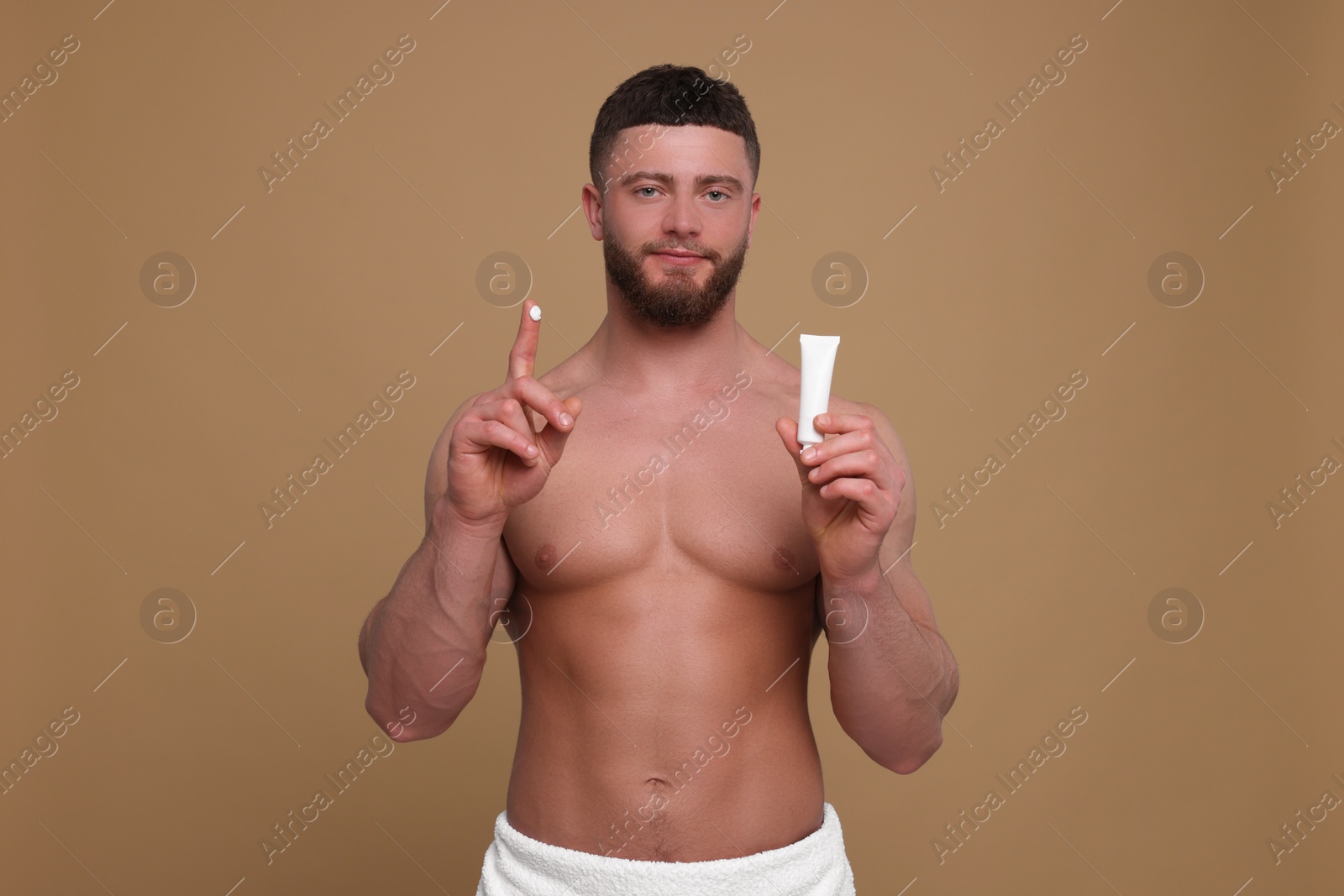 Photo of Handsome man with tube of body cream on pale brown background