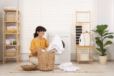 Photo of Happy woman with laundry near washing machine indoors