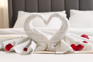 Honeymoon. Swans made of towels and rose petals on bed in room